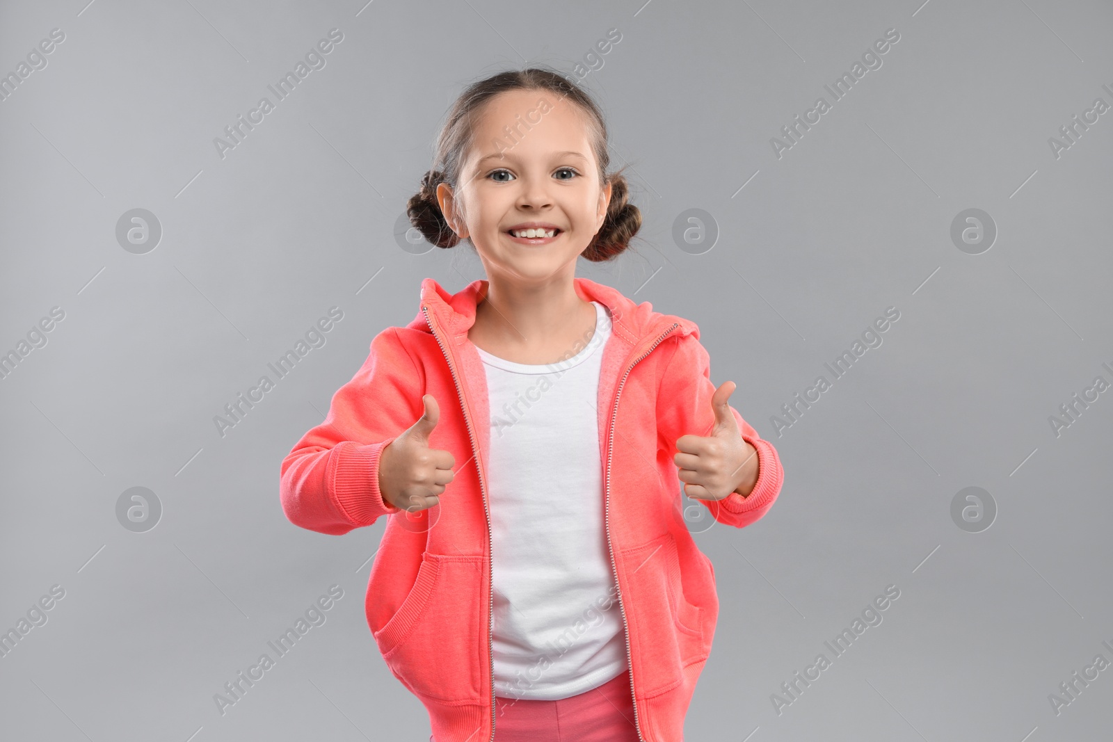 Photo of Cute little girl showing thumbs up on grey background