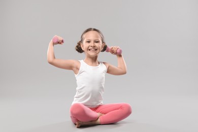 Cute little girl with dumbbells on grey background