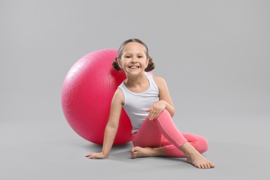 Cute little girl with fit ball on grey background