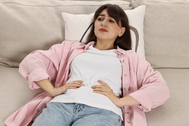 Photo of Upset woman suffering from abdominal pain on sofa at home