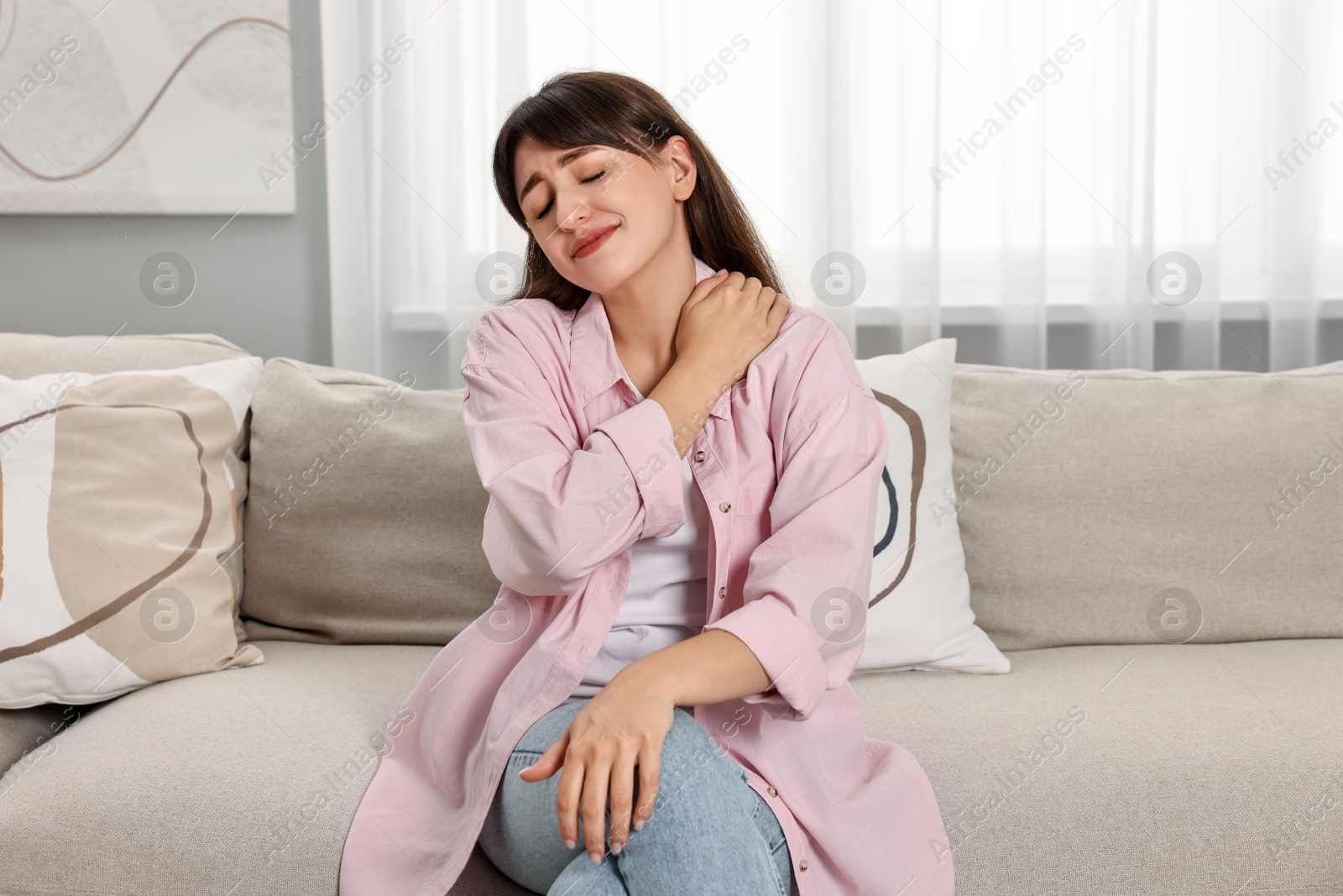 Photo of Upset woman suffering from neck pain on sofa at home