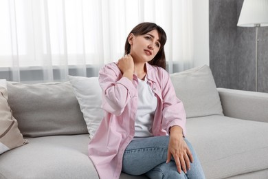 Upset woman suffering from neck pain on sofa at home