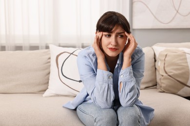 Upset woman suffering from headache on sofa at home