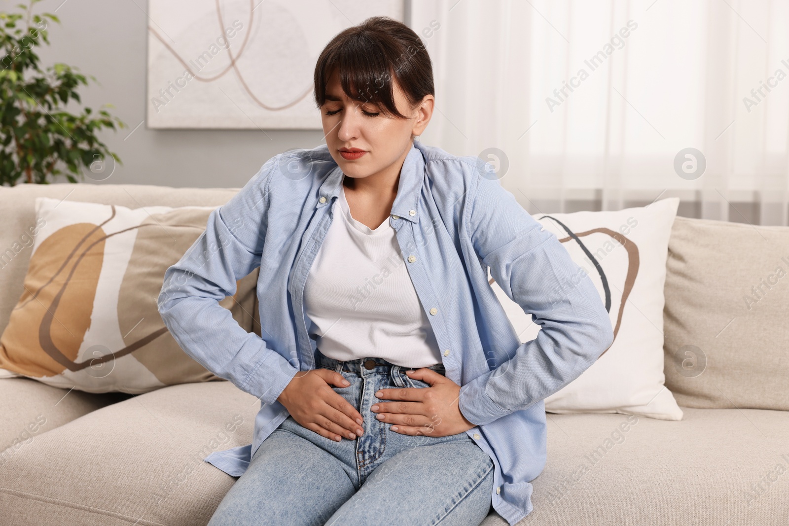Photo of Upset woman suffering from abdominal pain on sofa at home