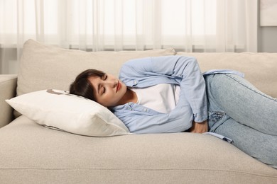 Upset woman suffering from abdominal pain on sofa at home