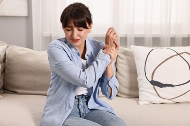 Photo of Upset woman suffering from pain in wrist on sofa at home