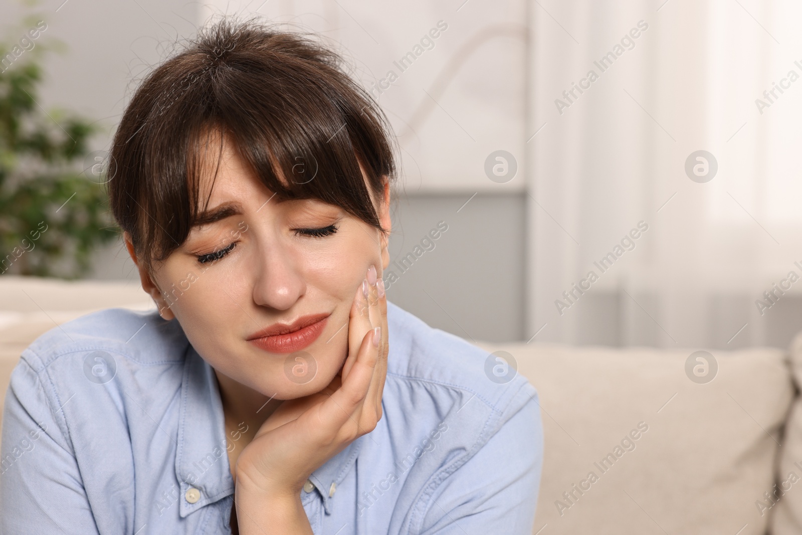 Photo of Upset young woman suffering from toothache indoors, space for text