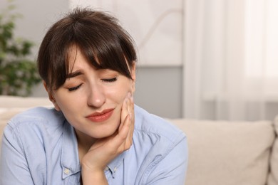 Upset young woman suffering from toothache indoors, space for text