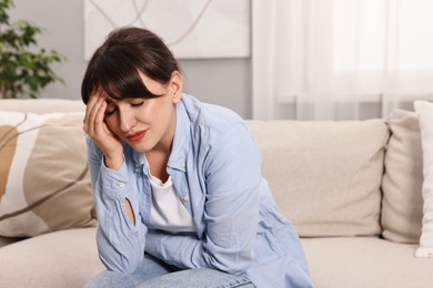 Photo of Upset woman suffering from abdominal pain on sofa at home