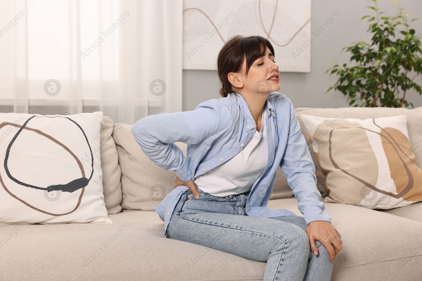 Photo of Upset woman suffering from back pain on sofa at home