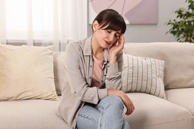 Upset woman suffering from headache on sofa at home