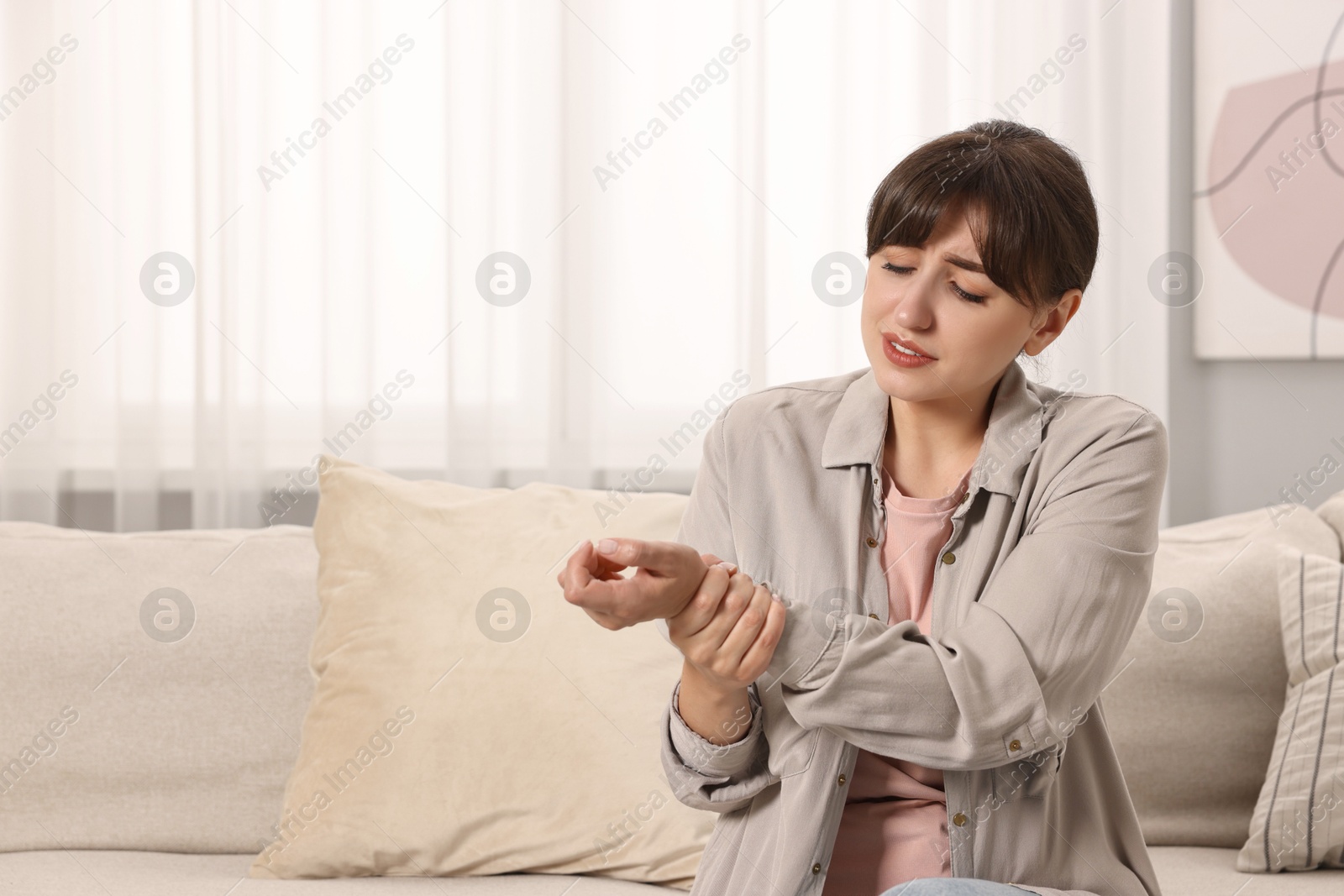 Photo of Upset woman suffering from pain in wrist on sofa at home, space for text