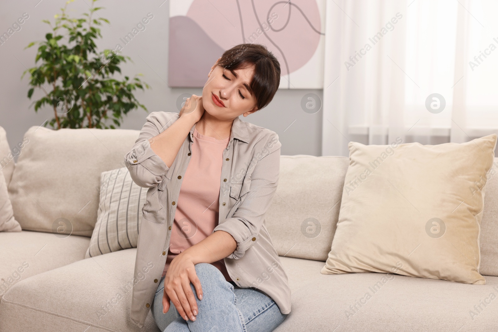 Photo of Upset woman suffering from neck pain on sofa at home