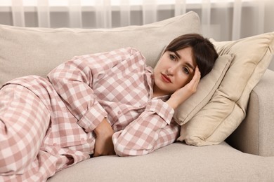 Upset woman suffering from abdominal pain on sofa at home