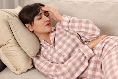 Upset woman suffering from headache on sofa at home