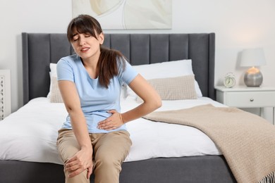 Upset woman suffering from abdominal pain on bed at home