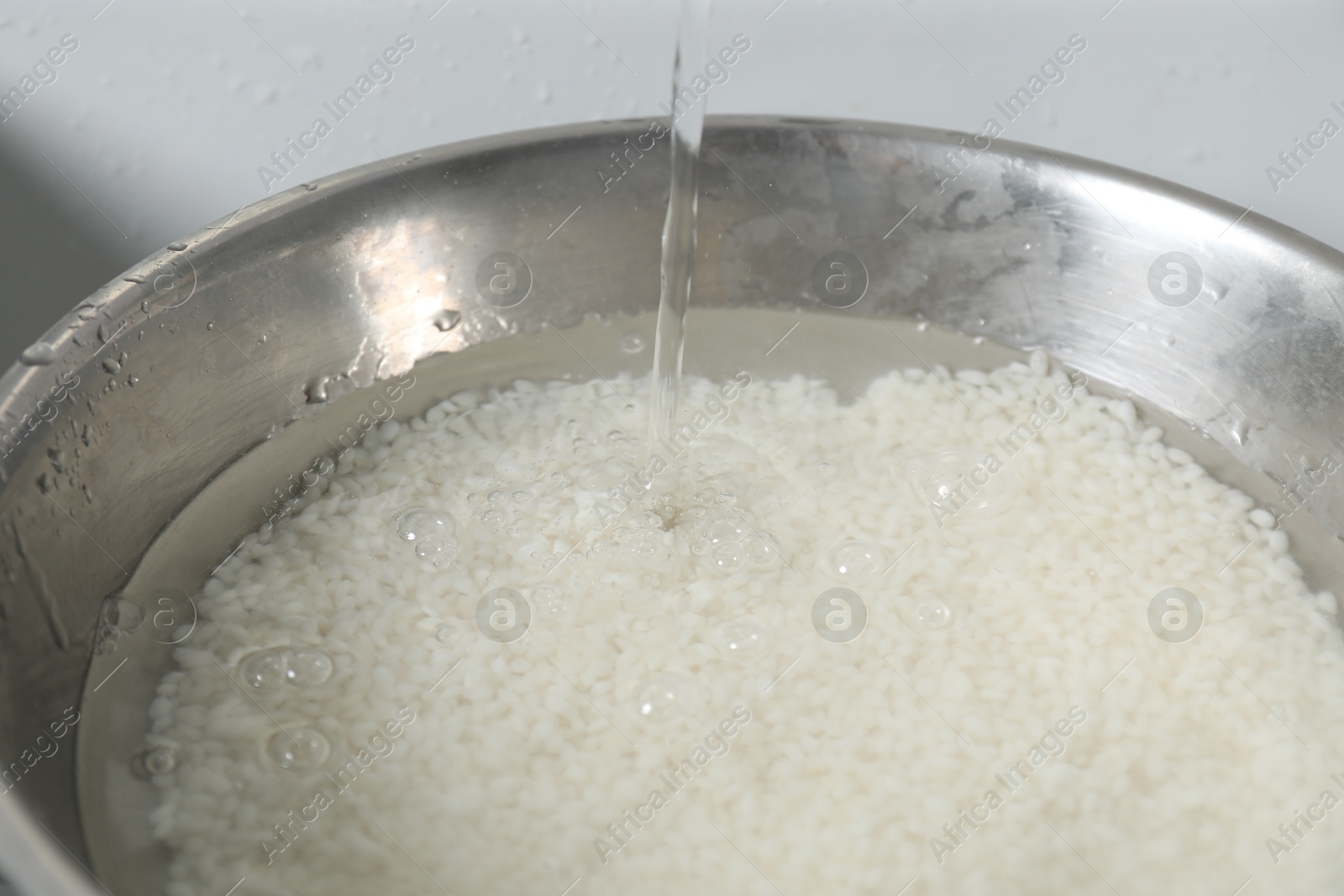 Photo of Pouring water into bowl with rice in sink, closeup