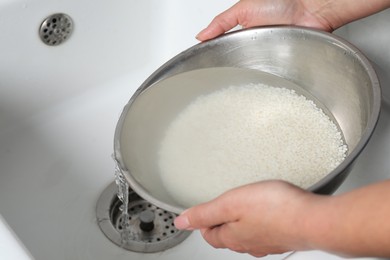 Photo of Woman rinsing rice in bowl above sink, closeup