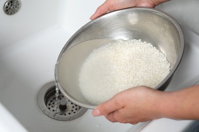 Photo of Woman rinsing rice in bowl above sink, closeup