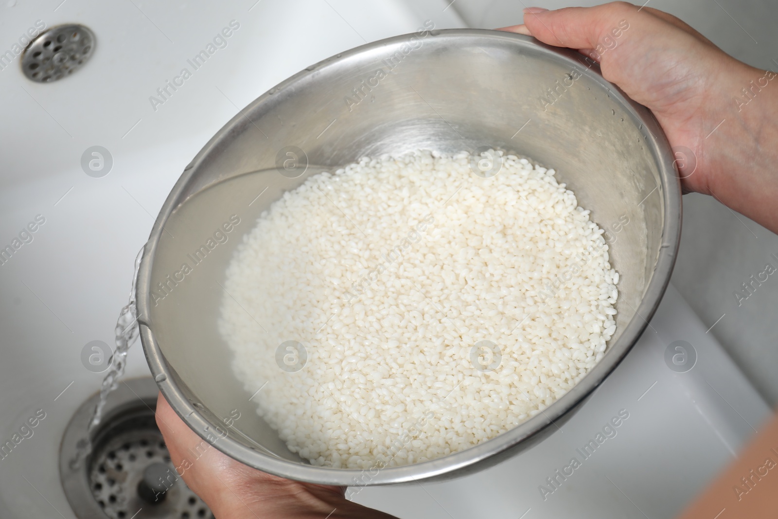 Photo of Woman rinsing rice in bowl above sink, closeup