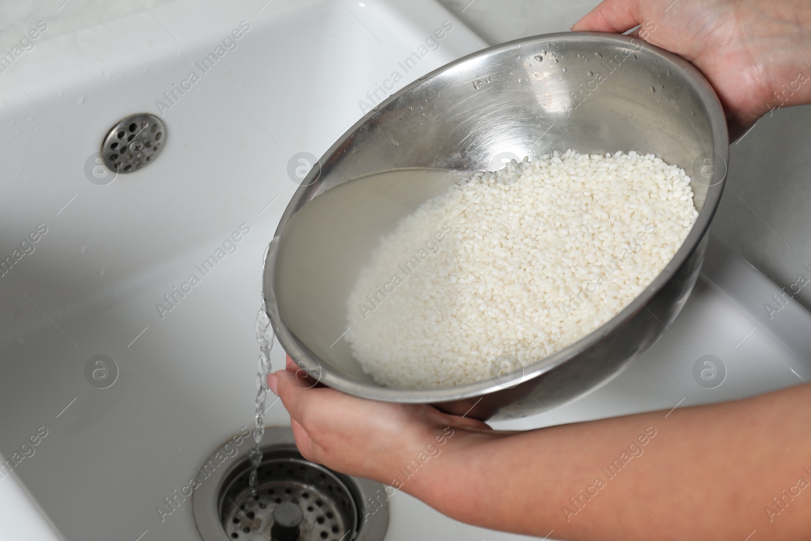 Photo of Woman rinsing rice in bowl above sink, closeup