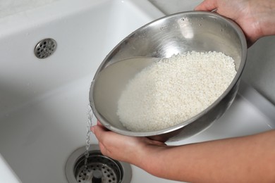 Photo of Woman rinsing rice in bowl above sink, closeup