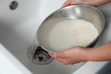 Photo of Woman rinsing rice in bowl above sink, closeup