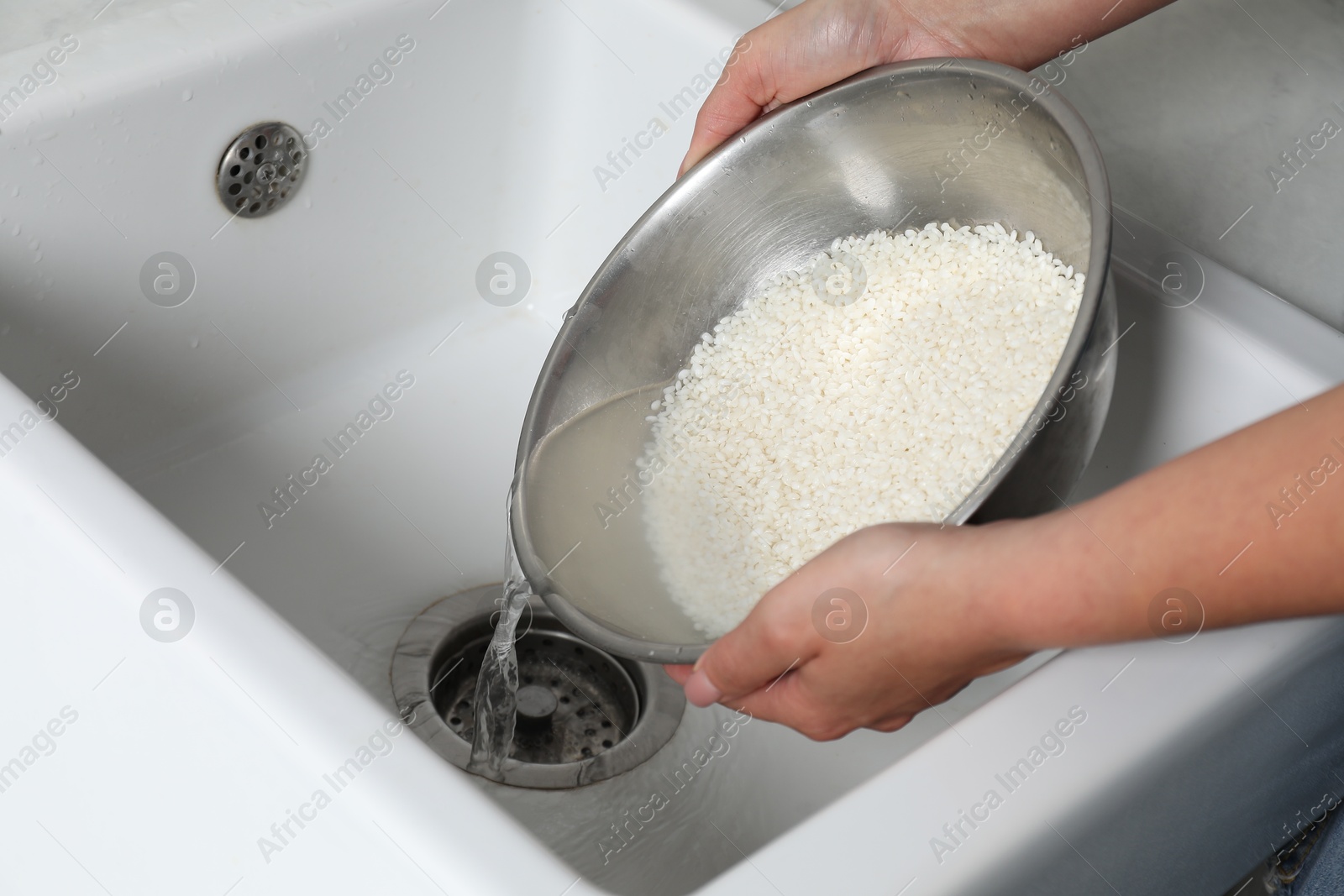 Photo of Woman rinsing rice in bowl above sink, closeup