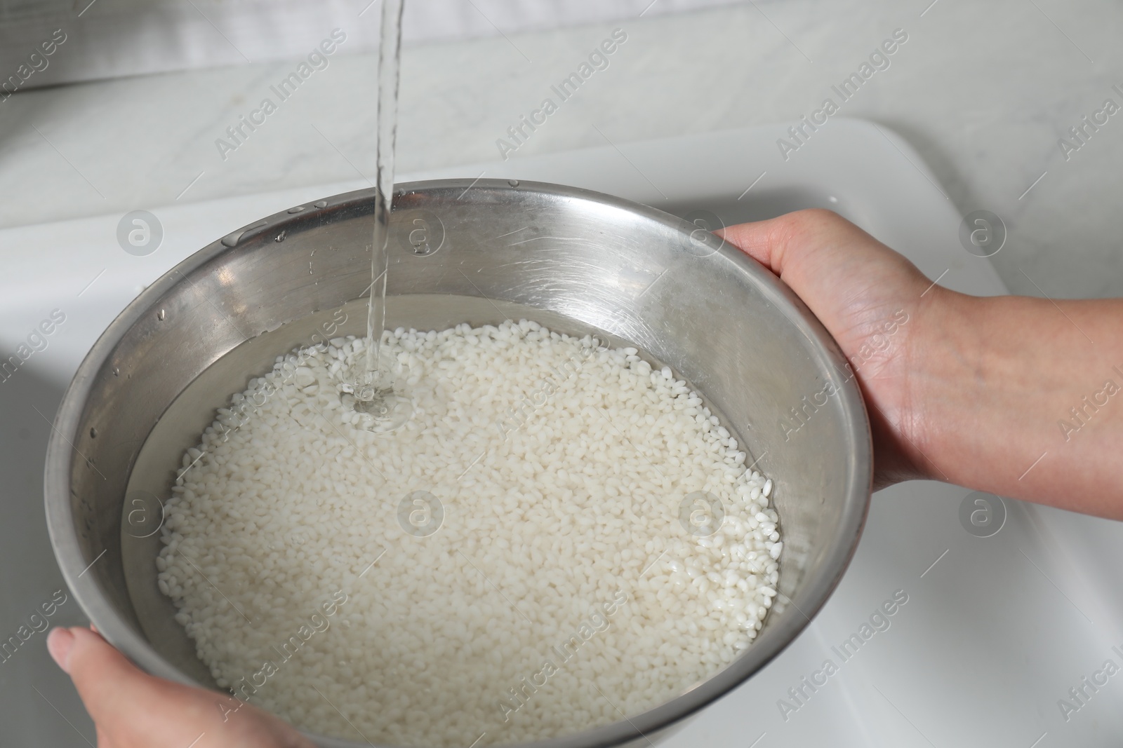 Photo of Woman rinsing rice in bowl above sink, closeup