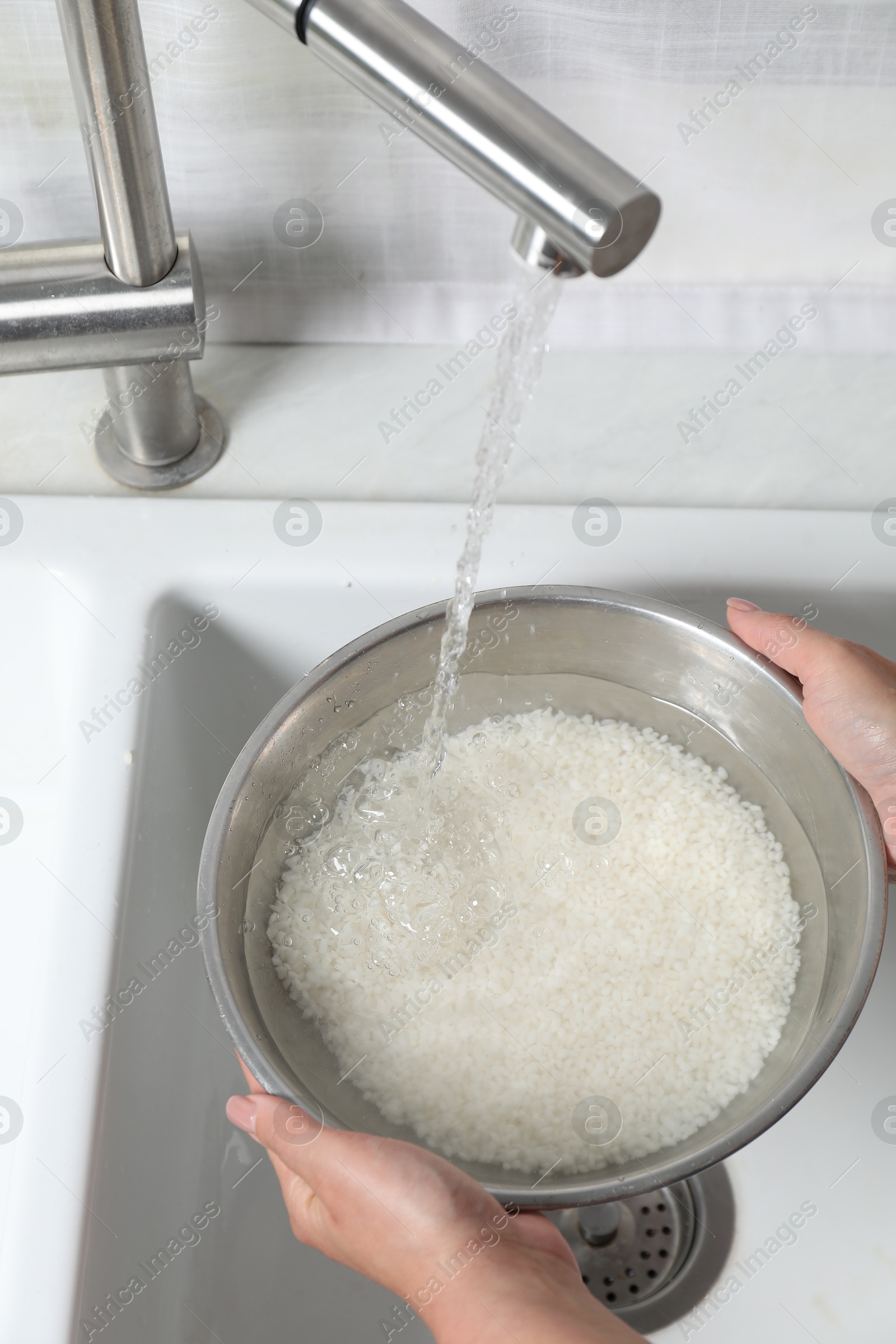 Photo of Woman rinsing rice in bowl above sink, closeup