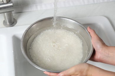 Photo of Woman rinsing rice in bowl above sink, closeup