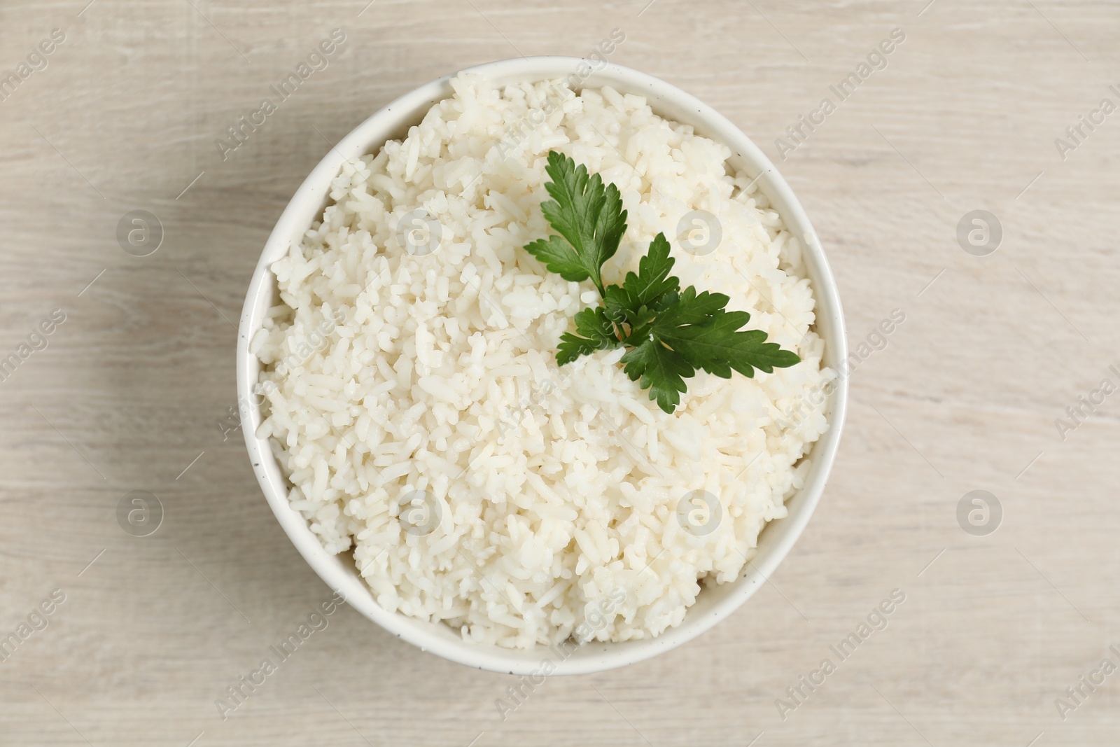 Photo of Delicious boiled rice in bowl and parsley on wooden table, top view