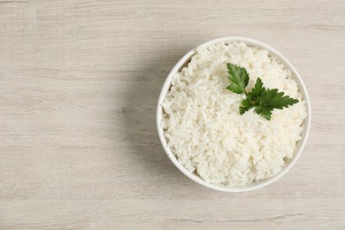 Photo of Delicious boiled rice in bowl and parsley on wooden table, top view. Space for text