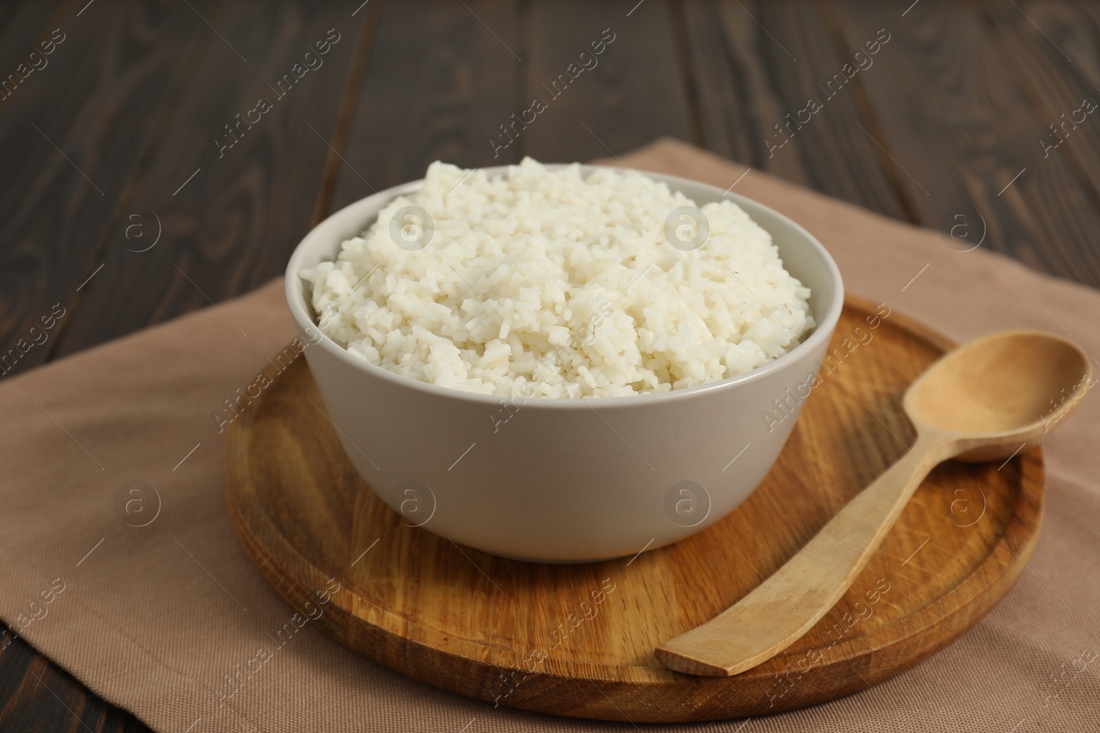 Photo of Delicious boiled rice in bowl and spoon on wooden table