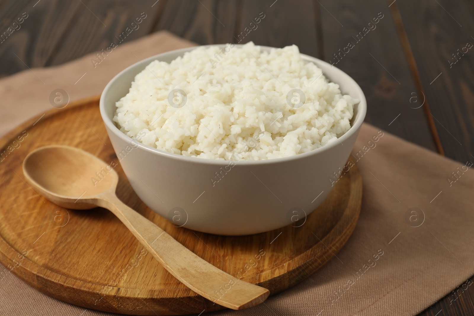 Photo of Delicious boiled rice in bowl and spoon on wooden table