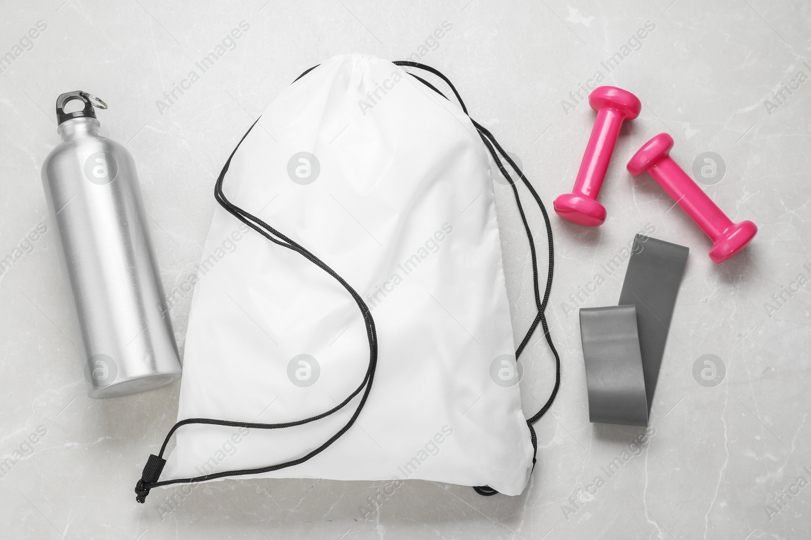 Photo of White drawstring bag, thermo bottle, fitness elastic band and dumbbells on light marble background, flat lay