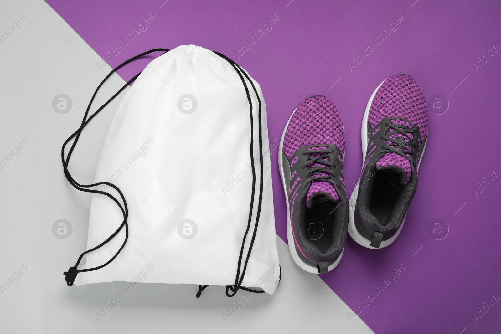 Photo of White drawstring bag and sneakers on color background, flat lay