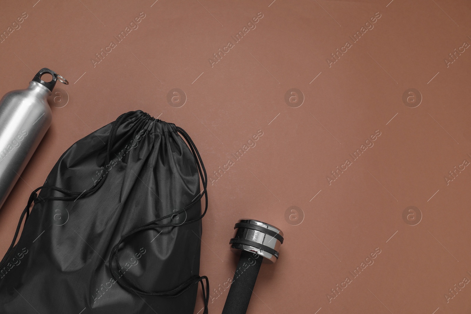Photo of Black drawstring bag, thermo bottle and dumbbell on brown background, flat lay. Space for text