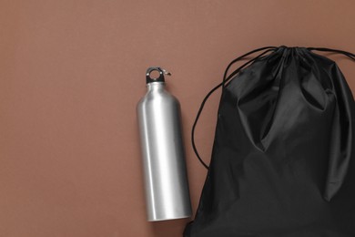 Photo of Black drawstring bag and thermo bottle on brown background, flat lay. Space for text