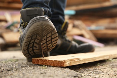 Photo of Careless worker stepping on nail in wooden plank outdoors, closeup