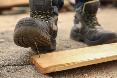 Careless worker stepping on nail in wooden plank outdoors, closeup