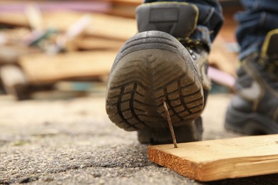 Careless worker stepping on nail in wooden plank outdoors, closeup. Space for text