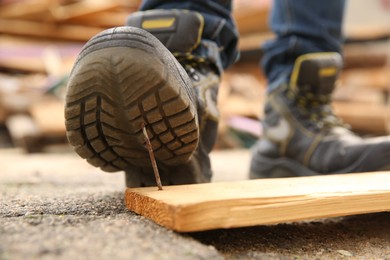 Careless worker stepping on nail in wooden plank outdoors, closeup