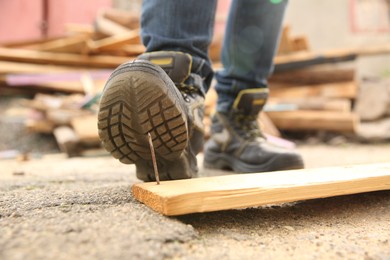 Photo of Careless worker stepping on nail in wooden plank outdoors, closeup