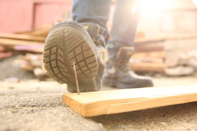 Careless worker stepping on nail in wooden plank outdoors, closeup