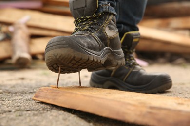 Photo of Careless worker stepping on nails in wooden plank outdoors, closeup