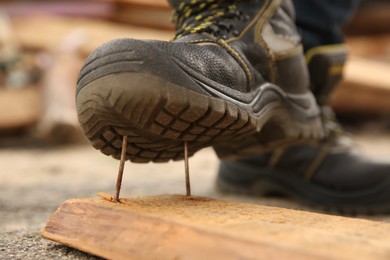 Photo of Careless worker stepping on nails in wooden plank outdoors, closeup