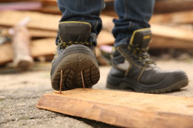 Careless worker stepping on nails in wooden plank outdoors, closeup