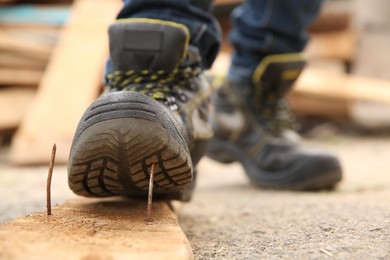 Careless worker stepping on nail in wooden plank outdoors, closeup