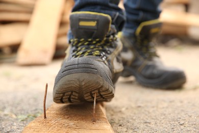 Careless worker stepping on nail in wooden plank outdoors, closeup